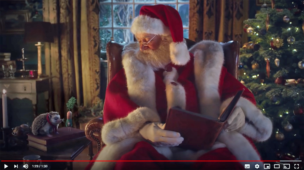 image shows Santa Claus reading a book to an animated hedgehog and carrot